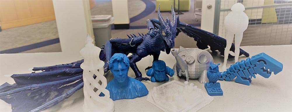 Various figurines 3d printed in shades of blue and gray: A tower with spiral base, a bust of a person, a dragon, Thanos head, owls, blocky t-rex skelton, and unusually shaped being with long skinny legs and a round body topped by a smaller jelly-fish shaped head
