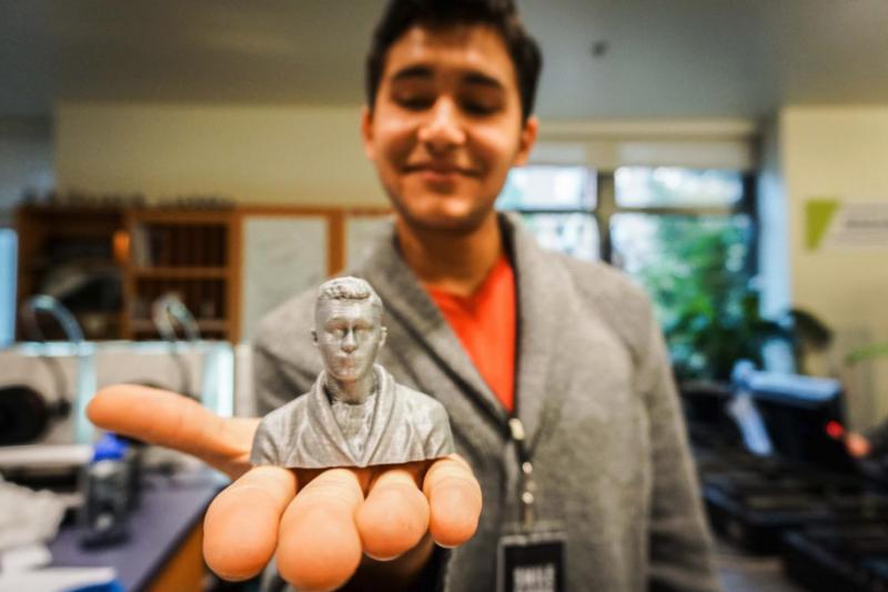 A student holds a silver 3d printed bust of themselves