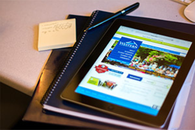A tablet with the Western Homepage loaded, on top of a spiral notebook and a black folder